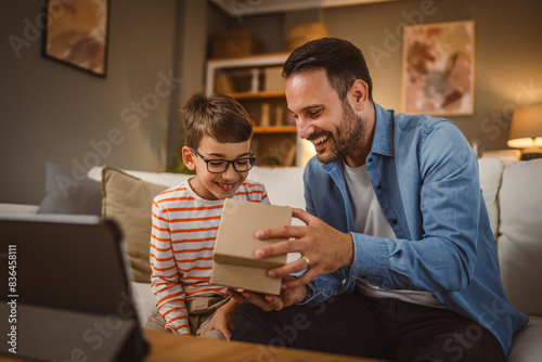 Father and son open birthday present home with tablet on the table