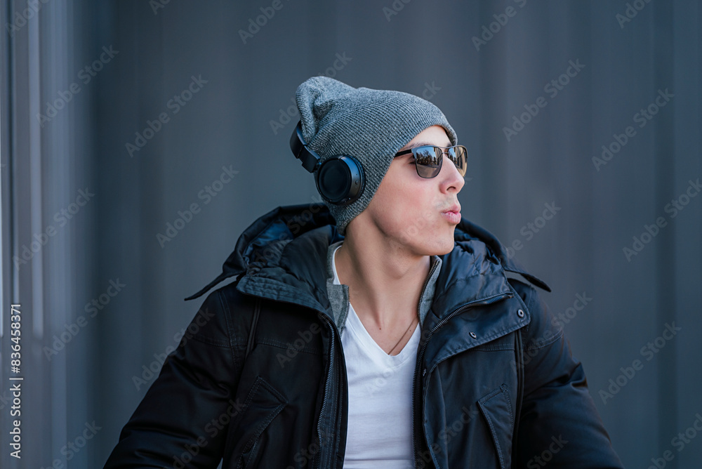 Portrait of Handsome Smiling Young Man with Woolen Hat, Sunglasses and Earphones on the Street Listening to Music Portrait of Handsome Smiling Young Man with Woolen Hat, Sunglasses and Earphones on the Street Listening to Music