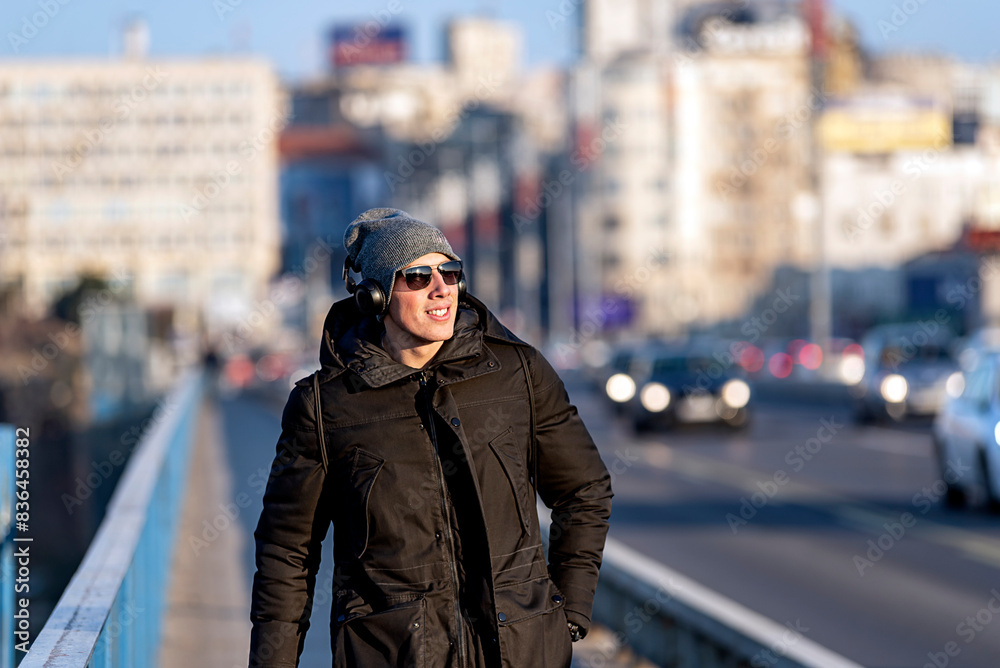 Portrait of Handsome Smiling Young Man with Woolen Hat, Sunglasses and Earphones on the Street Listening to Music Portrait of Handsome Smiling Young Man with Woolen Hat, Sunglasses and Earphones on the Street Listening to Music