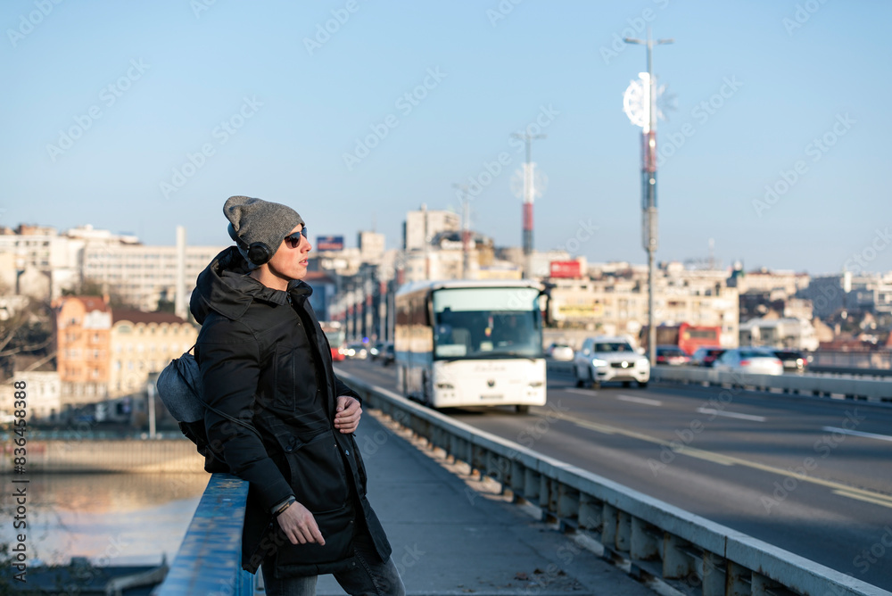Portrait of Handsome Smiling Young Man with Woolen Hat, Sunglasses and Earphones on the Street Listening to Music Portrait of Handsome Smiling Young Man with Woolen Hat, Sunglasses and Earphones on the Street Listening to Music