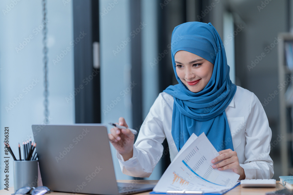 A female Arab entrepreneur is diligently working in her office, utilizing her laptop and documents to accomplish her tasks with contentment. A female Arab entrepreneur is diligently working in her office, utilizing her laptop and documents to accomplish her tasks with contentment.