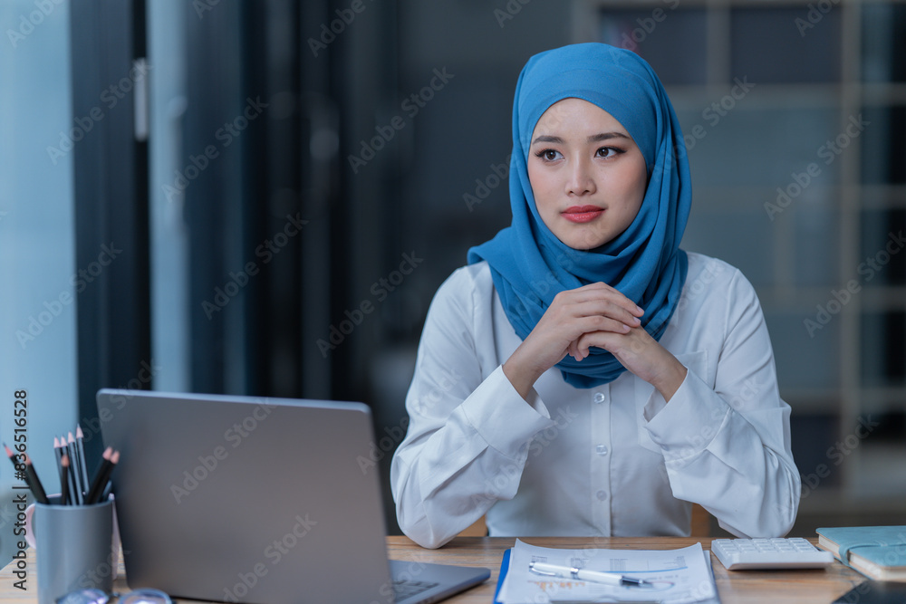 A female Arab entrepreneur is diligently working in her office, utilizing her laptop and documents to accomplish her tasks with contentment. A female Arab entrepreneur is diligently working in her office, utilizing her laptop and documents to accomplish her tasks with contentment.
