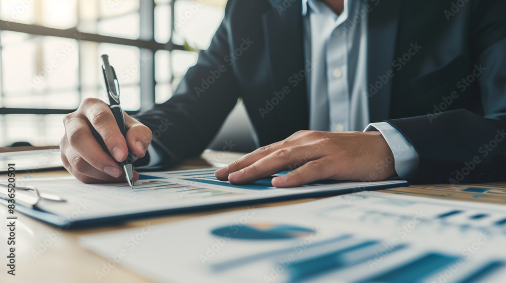 Naklejka premium a person engaged in work at a desk. The person is dressed in business attire, wearing a dark suit jacket over a light blue shirt. Their hands are focused on handling a pen and some papers