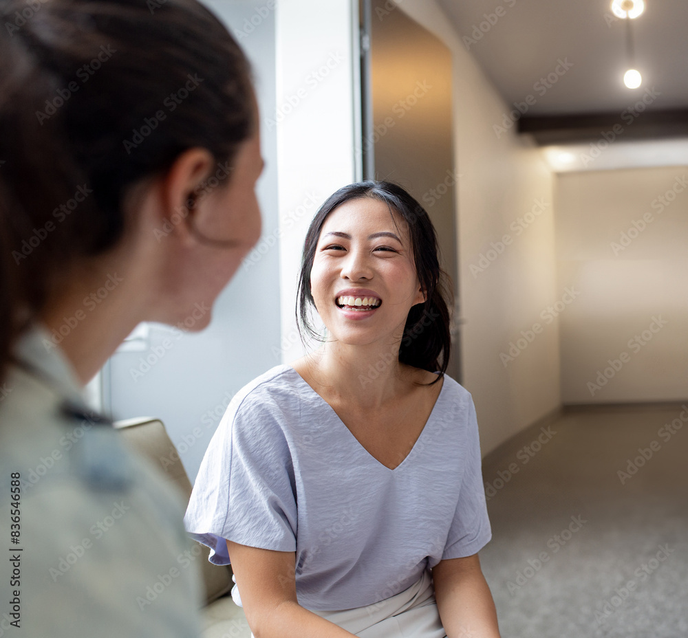 Asian woman smiling while talking to her colleague in an office Asian woman smiling while talking to her colleague in an office