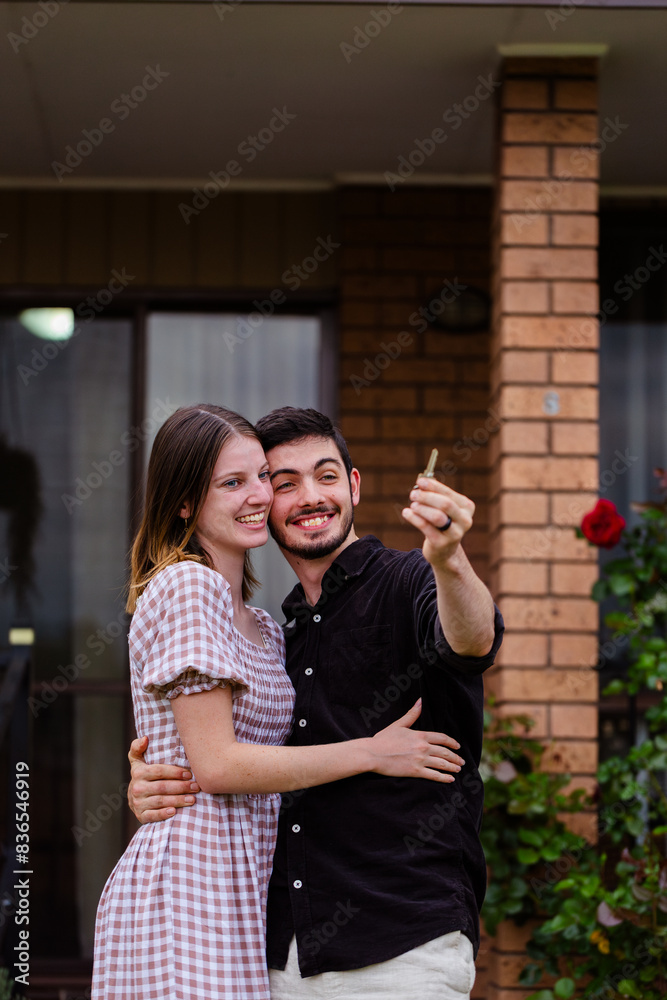 Young homeowners holding key first home hugging and smiling together Young homeowners holding key first home hugging and smiling together