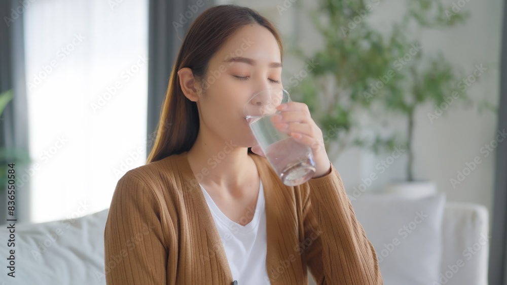 Happy young Asian woman drinking water while sitting on the sofa in the living room Happy young Asian woman drinking water while sitting on the sofa in the living room