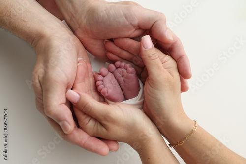 The palms of the father, the mother are holding the foot of the newborn baby in a white blanket. Feet of the newborn on the palms of the parents. Studio macro photo of a child's toes, heels and feet
