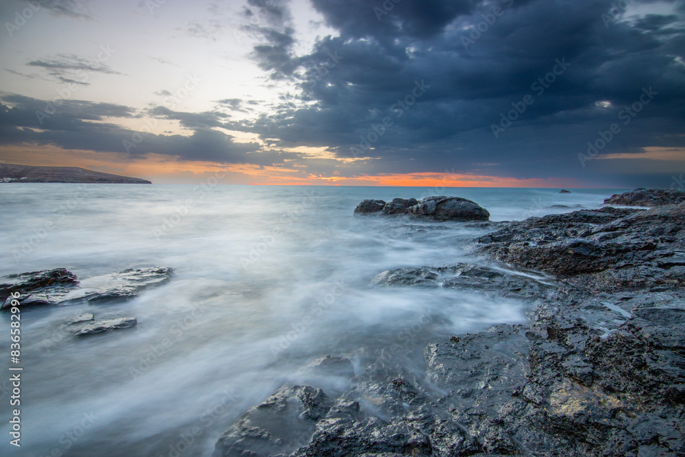 Sunrise with a sea view in a bay with a sandy beach and stones. rocky coast in warm colors. Landscape of Tarajalejo in Fuerteventura, Canary Islands, Spain. Sunrise with a sea view in a bay with a sandy beach and stones. rocky coast in warm colors. Landscape of Tarajalejo in Fuerteventura, Canary Islands, Spain.
