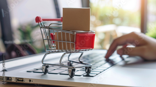 Digital online shopping concept, miniature cart with boxes on laptop keyboard and blurred web store interface background