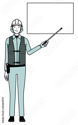 Senior female engineer in helmet and work wear pointing at a whiteboard with an indicator stick.