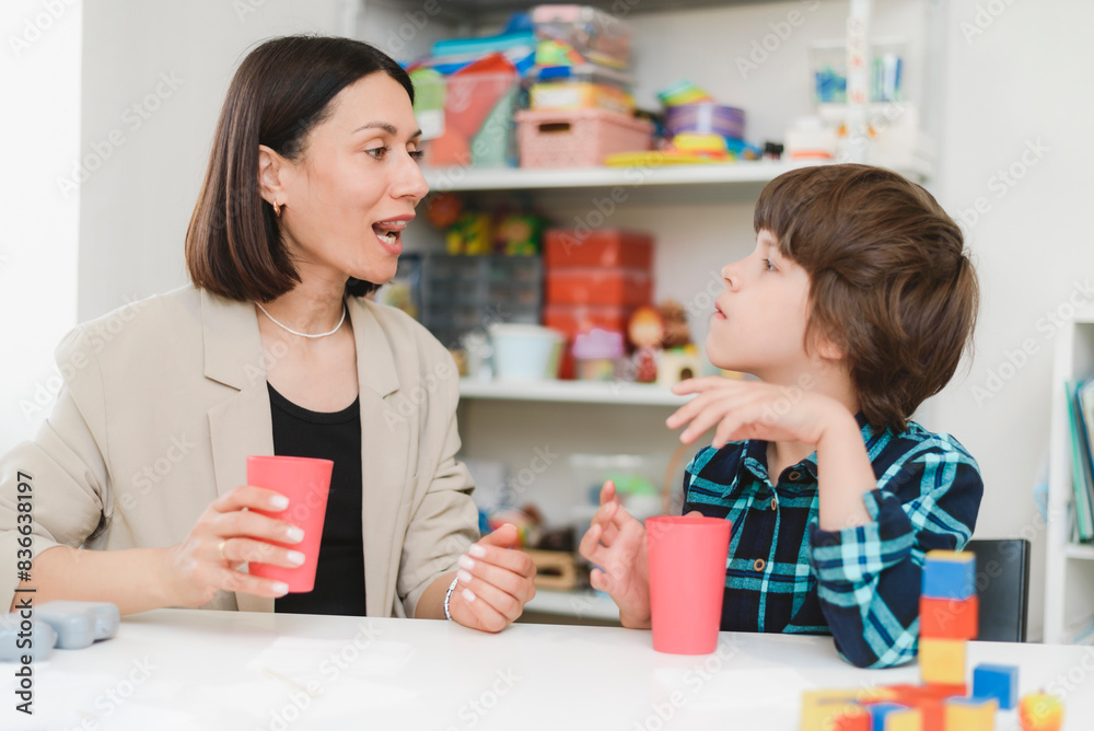 Obraz premium Beautiful woman speech therapist teaches boy the correct pronunciation of words and sounds in the office