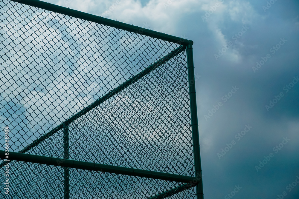A green metal fence with a cloudy sky in the background A green metal fence with a cloudy sky in the background