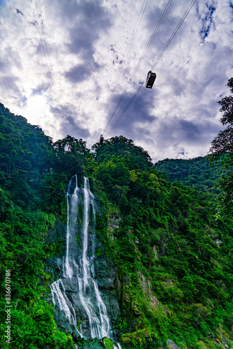 A waterfall is seen in the background of a photo with a cable car flying over it