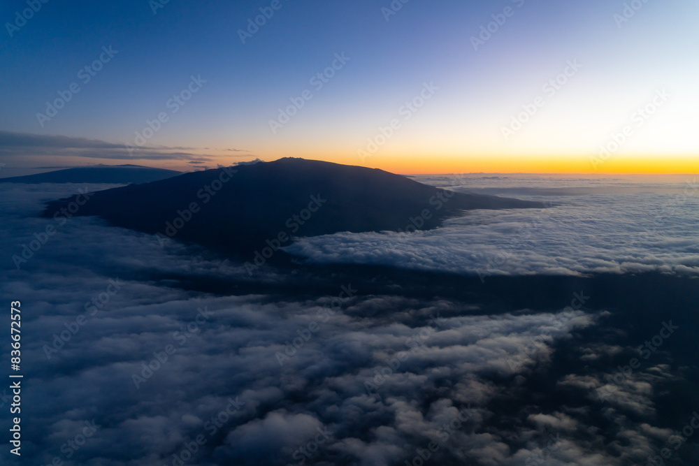 Aerial photo of Mauna Loa and Mauna Kea above the clouds at sunset. Flight from Hilo to Honolulu.