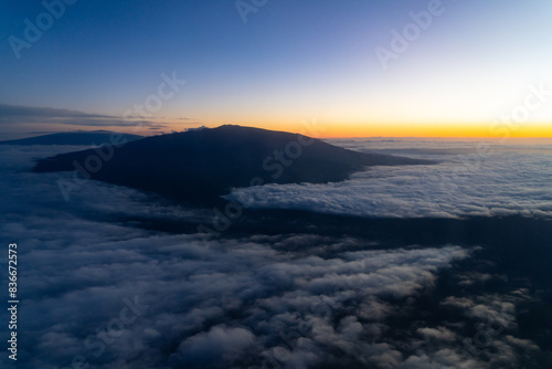 Aerial photo of Mauna Loa and Mauna Kea above the clouds at sunset. Flight from Hilo to Honolulu.