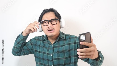 Footage of adult Asian man showing can not hear to someone gesture when listening music