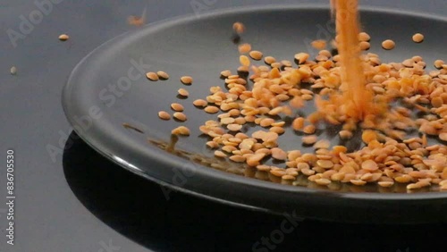 red lentils falling on dark plate, video