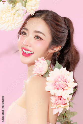 Pretty Asian beauty woman with Korean makeup glowing face and healthy facial skin portrait smile holding flower on isolated pink background. Cosmetology ,Plastic surgery.