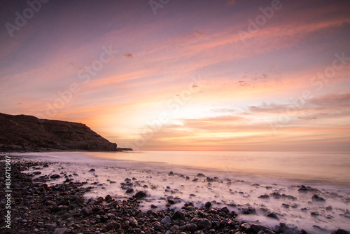 Sunrise with sea view in a secluded bay. rocky coast in warm colors. Landscape with a lava stone beach at Tarajalejo on Fuerteventura, Canary Islands, Spain.