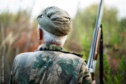 Rear view of a mature male with a camouflage outfit and a gun in a forest