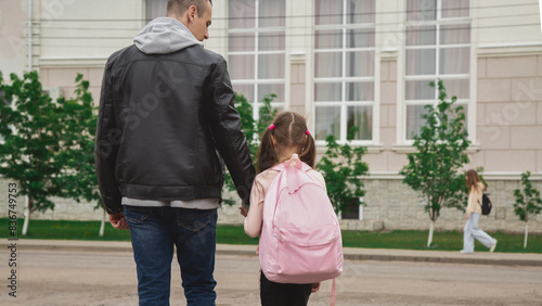 Back to school. Schoolgirl with backpack and father going to school first lesson holding hands back view close up. Man dad and daughter kid walking outdoor schoolyard © Mariia