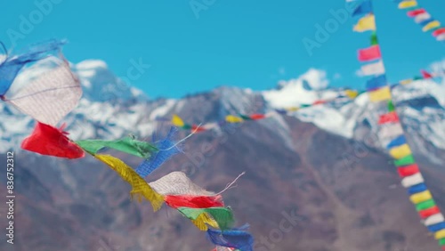 Slow motion shot of Buddhist prayer flags waving in the wind in front of the snow covered Himalayan mountain peaks as seen from Padum in Ladakh, India. Religious prayer flags wave against the blue sky