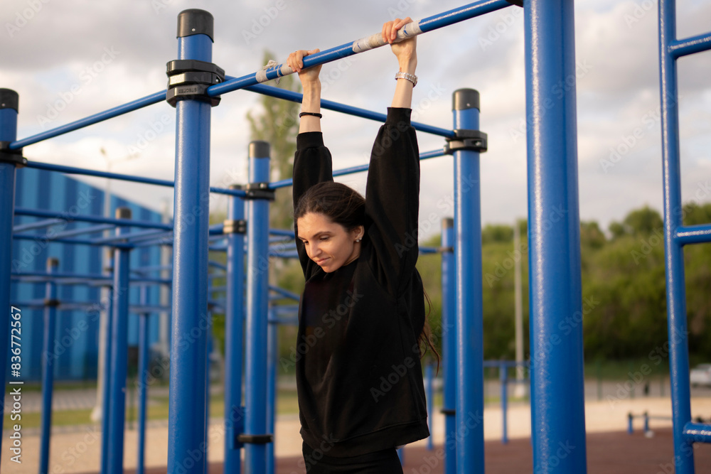 Obraz premium Young Female Athlete Hanging on the Bar on Outdoor Exercise Equipment