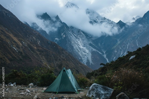 Solitary tent set up in a majestic mountain valley with clouds descending onto the peaks