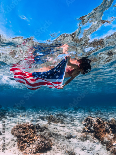 Woman snorkeling underwater in blue sea with US flag. Independence day concept.