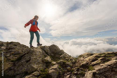 A woman in a red jacket is standing on a rocky mountain top