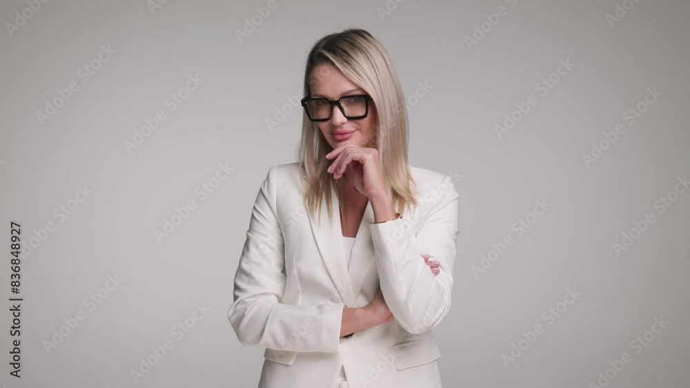 pensive businesswoman in white suit is looking to side while smiling and stading on gray studio background pensive businesswoman in white suit is looking to side while smiling and stading on gray studio background