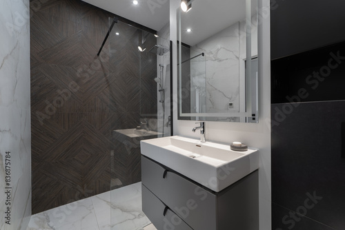 A beautifully designed modern bathroom featuring a glass-enclosed shower  elegant vanity with large mirror  and sleek fixtures. The space combines dark and light tones for a sophisticated look.