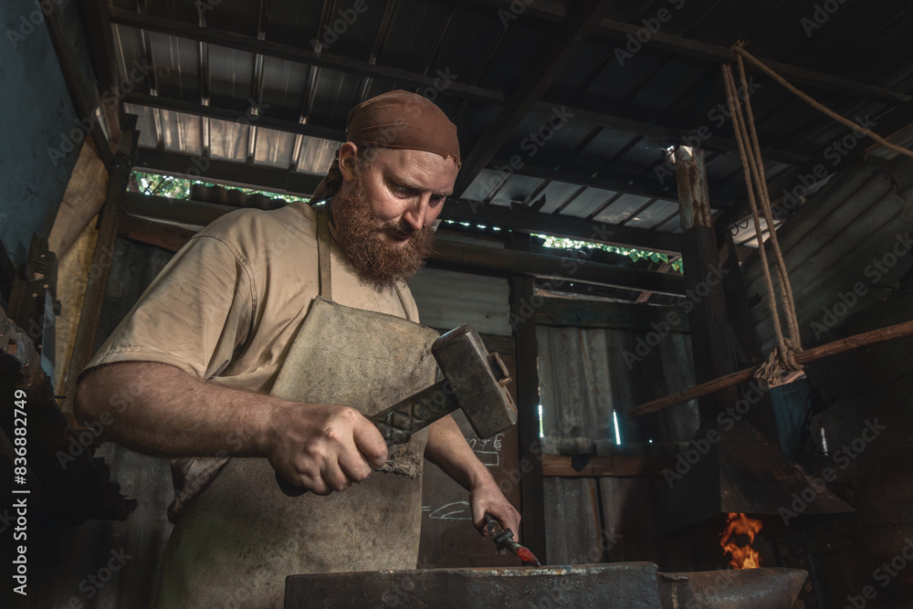 Blacksmith forges a red-hot metal piece on an anvil in a rural forge. Traditional crafts Blacksmith forges a red-hot metal piece on an anvil in a rural forge. Traditional crafts
