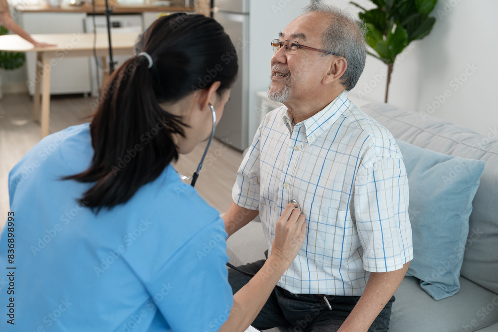 Obraz premium Asian young woman caregiver doctor using stethoscope to checking heartbeat elderly man patient in room during home visit