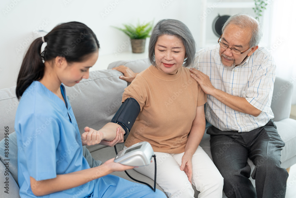 Obraz premium Asian caregiver doctor using digital pressure gauge measuring blood pressure of elderly woman patient Young female nurse in uniform gives consultation during home visit.