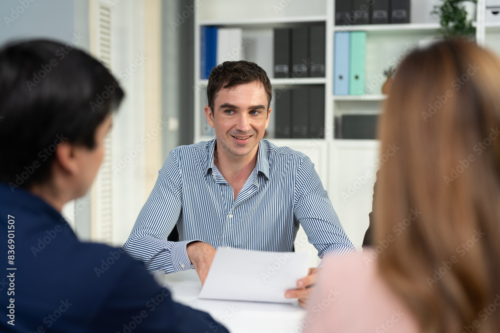 Smiling manager leading a discussion with two colleagues in an office setting, holding documents and engaging in conversation. Smiling manager leading a discussion with two colleagues in an office setting, holding documents and engaging in conversation.