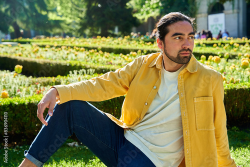 A man in a yellow shirt and blue jeans is sitting in a park. He is wearing a white shirt and has a beard photo