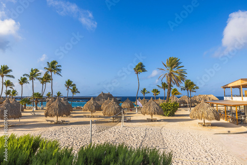 Fototapeta Naklejka Na Ścianę i Meble -  Spectacular view of the hotel's sandy beach with sun loungers, sunshades, palm trees, and volleyball court by the Caribbean Sea. Curaçao.