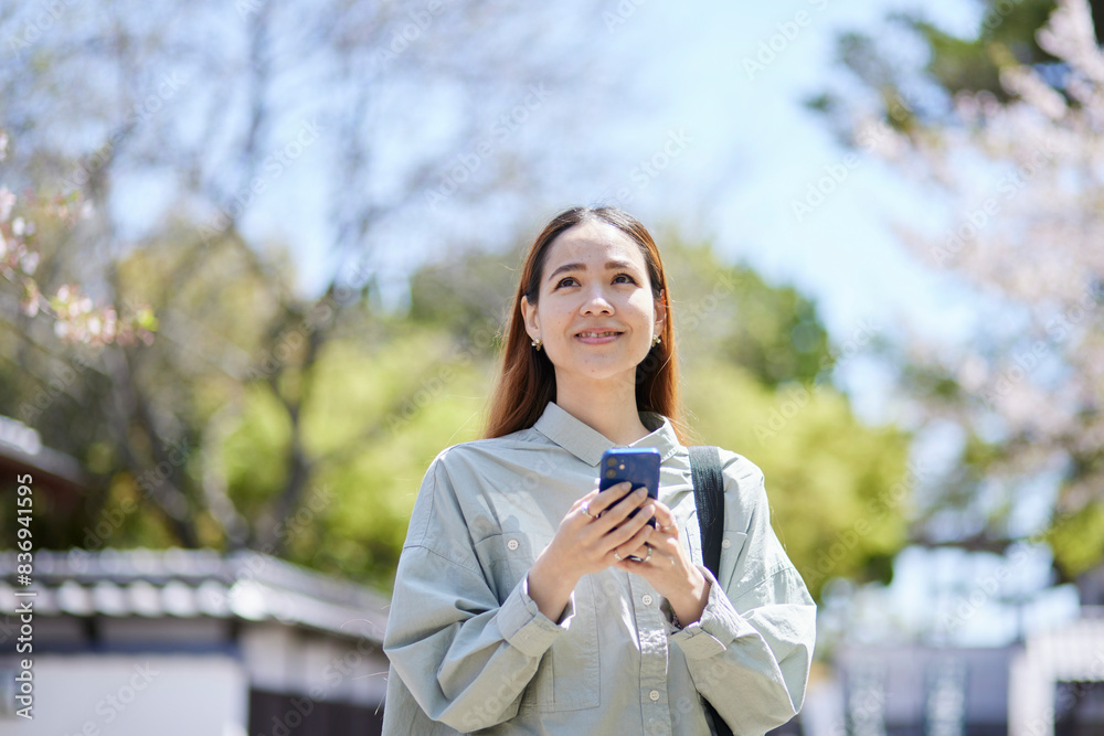 春の観光地でスマートフォンを持つインバウンド旅行者の女性 春の観光地でスマートフォンを持つインバウンド旅行者の女性