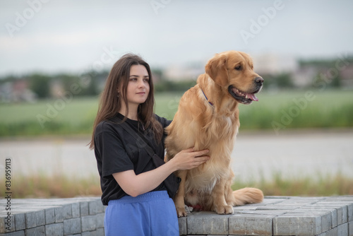 A beautiful young dark-haired girl walks with a purebred retriever in nature.