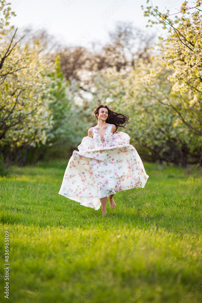 Full-length portrait of a beautiful brunette caucasian woman running in blossoming apple garden in white floral dress on a fresh green grass shot from her face with her hair flying Full-length portrait of a beautiful brunette caucasian woman running in blossoming apple garden in white floral dress on a fresh green grass shot from her face with her hair flying