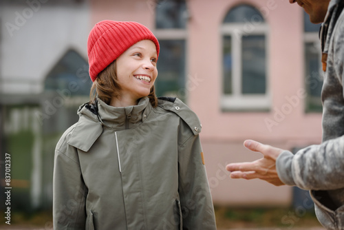 Cheerful smiling young boy talking with school teacher outdoor, Joyful connection: Young boy smiles, engaging in a cheerful conversation with his school teacher outdoors.