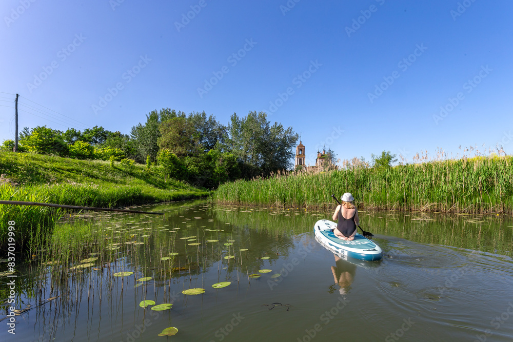 Fototapeta premium Suzdal, Russia, Golden Ring: A tourist girl swims along the river past the sights of the ancient Russian city of Suzdal in the warm summer