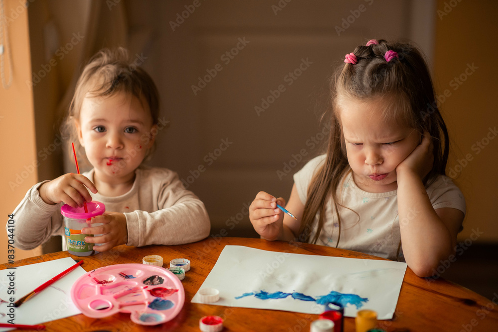 Fototapeta premium two sisters paint with paints, one is 1 year old and the older one is 5 years old.