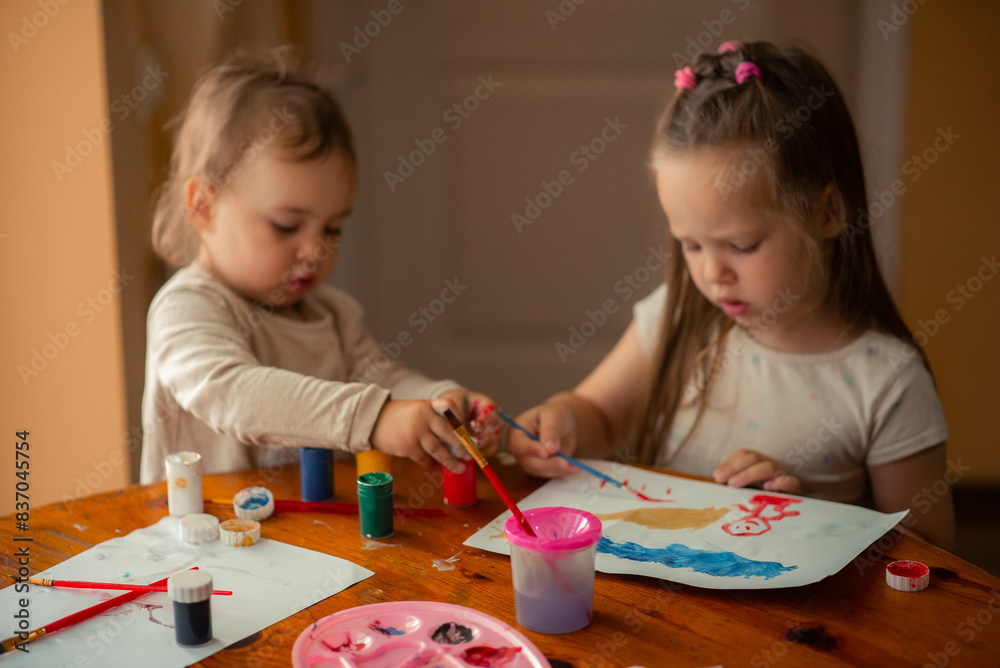 Fototapeta premium two sisters paint with paints, one is 1 year old and the older one is 5 years old.