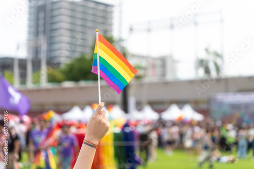 Close up hand holding rainbow flag raise up for freedom with LGBT pride month festival background. Demonstrate rights LGBTQ celebration pride Month lesbian pride symbol. Bangkok Pride Month festival.