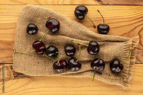 Several ripe sweet cherries with jute bag on wooden table, macro, top view.