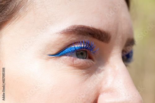 Close-up of a woman's eye with blue eyeliner and mascara, showcasing vibrant makeup details.
