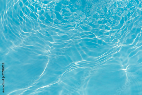 Blue water with ripples on the surface. Defocus blurred transparent blue colored clear calm water surface texture with splashes and bubbles. Water waves with shining pattern texture background.