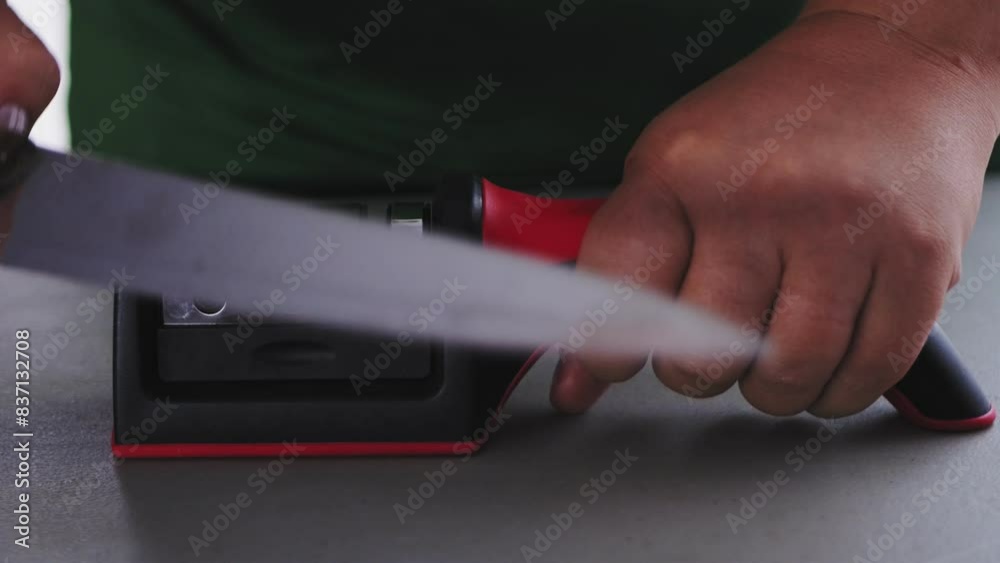 a kitchen knife in the cook's hand is sharpened in a special knife sharpener on the table a kitchen knife in the cook's hand is sharpened in a special knife sharpener on the table